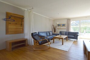 Een moderne woonkamer met twee banken, een schommelstoel, een salontafel en een houten bankje.