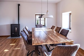 Un comedor espacioso con una larga mesa de madera, sillas de cuero, una lámpara colgante y un estufa de leña negra.