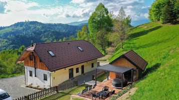 A two-story house with a patio area, a covered outdoor seating space, and a view of a mountainous landscape.