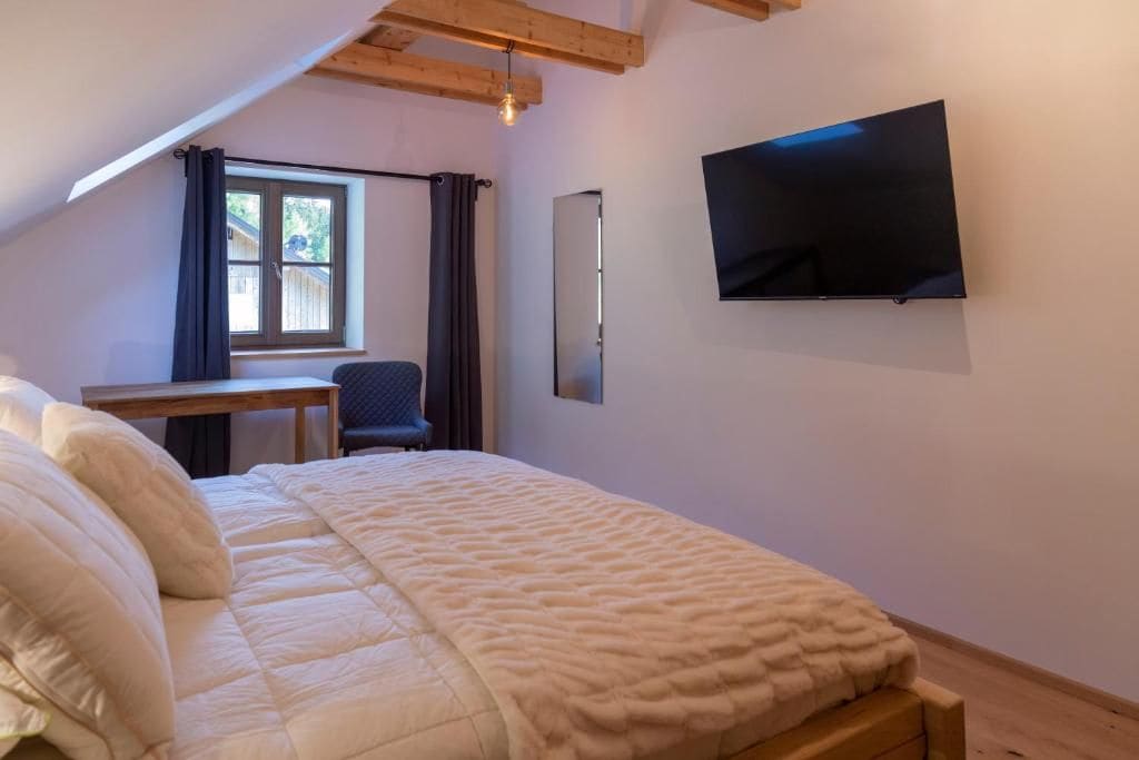 A bedroom with a bed, a desk, a chair, a TV, and a window with curtains.