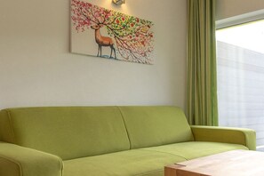 A green sofa in a room with a wall-mounted painting of a deer and tree. - Bungis holiday home directly on the lake, H13 (Joachimsthal)