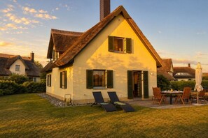Ein Haus mit einem Reetdach, einer gelben Fassade und einer Terrasse mit Gartenmöbeln.