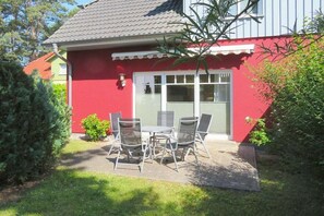 Ein rotes Gebäude mit einer weißen Tür und einer kleinen Terrasse mit Tisch und Stühlen.