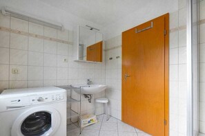 Ein kleines Badezimmer mit Waschmaschine, Waschbecken und Spiegel.