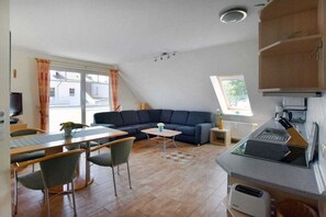 Ein Wohnzimmer mit einer Couch, einem Esstisch, Stühlen, einem kleinen Couchtisch und einer Küchenzeile.