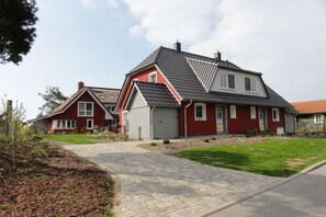 A residential area with a paved driveway leading to a red house with a grey roof. - Holiday home Wiecker Landhus | FHH 2 (Wieck)