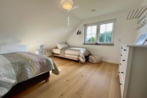 A bedroom with a sloped ceiling, a bed, a bedside table, a window, and a wardrobe. - Thatched House Mellnitz (Mellnitz)