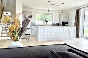 A modern kitchen with white cabinets, a central island, and a dining area with a dark rug. - Thatched House Mellnitz (Mellnitz)
