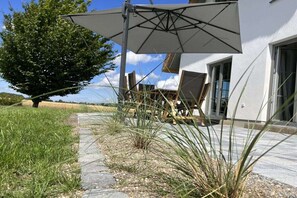 A patio area with a large umbrella, a tree, and a building with a glass door. - Thatched House Mellnitz (Mellnitz)