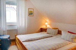 Ein Schlafzimmer mit zwei Betten, einem Nachttisch mit Lampe, einem Heizkörper und einem Fenster mit Vorhängen.