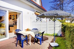 Eine Terrasse mit Tisch und Stühlen, ein weißer Zaun und ein großer Sonnenschirm.