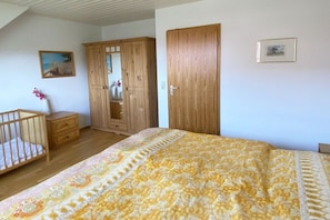 A bedroom with a bed, a wooden wardrobe, a wooden cabinet, a crib, and a framed picture on the wall. - Terraced house with 1 bedroom (Ostseebad Prerow)