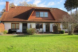 Ein zweistöckiges Haus mit geneigtem Dach, einem Schornstein und einer Veranda mit Tisch und Stühlen.