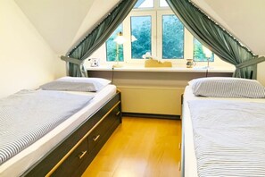 A bedroom with two beds, a window with curtains, a desk, and a lamp. - Captain's Garden W13 "Roth" (Prerow)