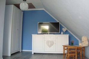 A room with a white cabinet, a flat-screen TV, a heart-shaped decoration, a teddy bear, and a small table. - Holiday home with 2 bedrooms (Rosenthal-Bielatal OT Bielatal)