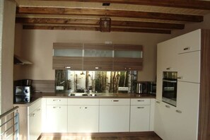 A modern kitchen with white cabinets, a wooden ceiling, and a large window with a view of trees. - Holiday home with 2 bedrooms (Rosenthal-Bielatal OT Bielatal)