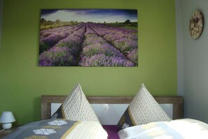 Een slaapkamer met een bed, kussens, een wandklok en een schilderij van lavendelvelden.