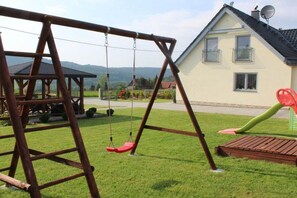 A wooden swing set and a slide in a grassy yard with a house in the background. - Holiday home with 2 bedrooms (Rosenthal-Bielatal OT Bielatal)