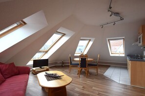 A loft-style room with a dining area, a red couch, and a kitchen area. - House "Am Brunnen" Where 7 (Ostseebad Prerow)