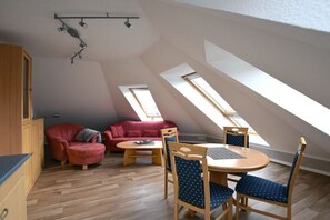 A loft-style room with a sloped ceiling, a dining table with chairs, a red sofa, and a small kitchenette area. - House "Am Brunnen" Where 7 (Ostseebad Prerow)