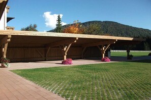 A covered outdoor area with a wooden structure, a paved walkway, and a grassy lawn. - in the Witting house (Leutasch)