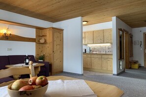 A room with a wooden ceiling, a dining table with a bowl of fruit, a purple sofa, and wooden cabinets. - in the Witting house (Leutasch)