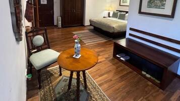 Una sala de estar con sofá, una mesa de centro, una silla, un mueble para televisión y un cuadro enmarcado en la pared.