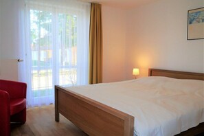 Habitació d'hotel amb un llit, una cadira, una làmpada i una porta que dona a una zona exterior.