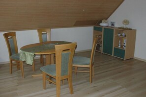 Ein Essbereich mit Holztisch und -stühlen, einer grünen Tischdecke und einer Holzvitrine mit Dekorationen.
