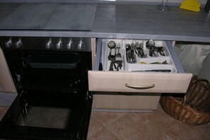 Eine Küche mit einem offenen Backofen und einer Schublade voller Küchenutensilien.