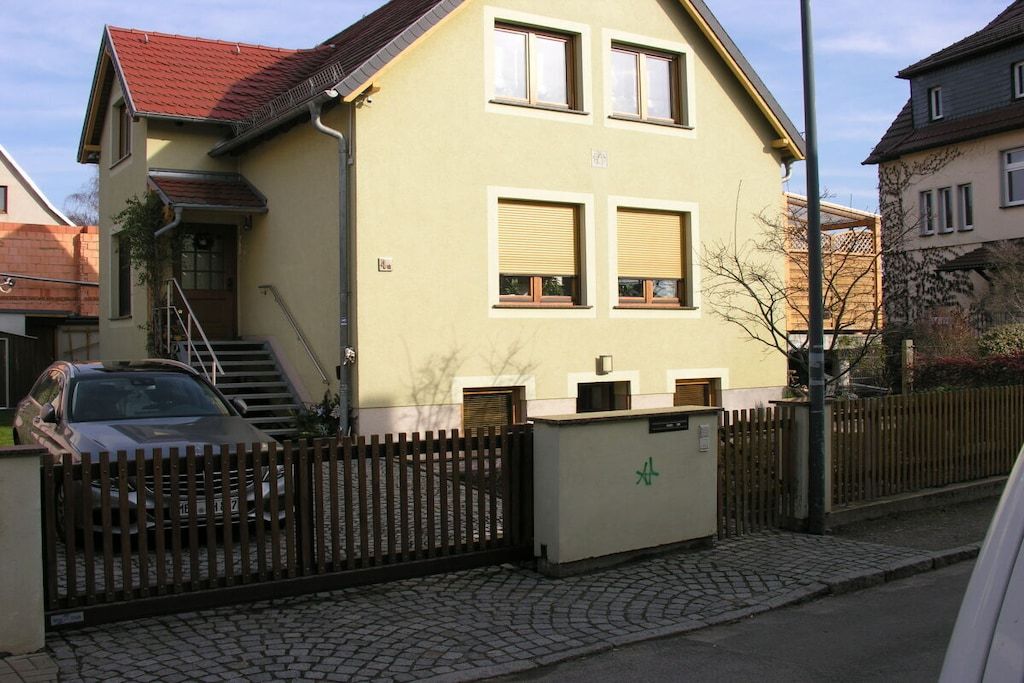 A two-story building with a red roof, a car parked in front, and a wooden fence.