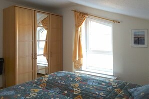 A bedroom with a bed, a wardrobe, a window with curtains, and a framed picture on the wall. - Holiday apartment with 2 bedrooms (Prerow)