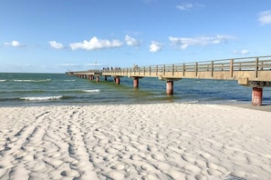 Une jetée qui s’avance dans la mer, avec une plage de sable au premier plan.