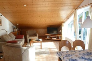A cozy living room with a wooden ceiling, a sofa, a coffee table, a TV, and a window with curtains. - Holiday apartment with 2 bedrooms (Prerow)