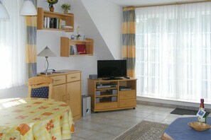 Ein Hotelzimmer mit einem Bett, einem Fernseher, einem Schreibtisch mit Lampe, einem Bücherregal und einem Fenster mit Vorhängen.