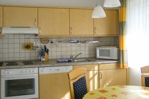 A kitchen with wooden cabinets, a microwave, a stove, and a sink. - Holiday apartment with 1 bedroom (Ostseebad Prerow)