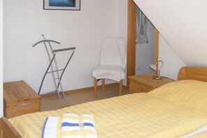 Een slaapkamer met een bed, een stoel, een nachtkastje, een lamp en een droogrek.