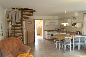 A compact living space with a spiral staircase, a dining area with chairs, a kitchen with a microwave, and a visible door leading to another room. - Terraced house with 2 bedrooms (Ostseebad Prerow)
