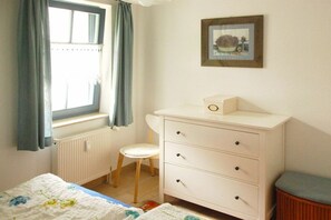 Ein Schlafzimmer mit einem Bett, einem Schminktisch, einem Stuhl, einem Heizkörper und einem Fenster mit Vorhängen.