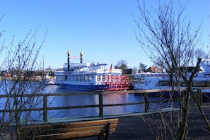 A riverfront with a large boat docked, a wooden bench, and leafless trees. - Terraced house with 2 bedrooms (Ostseebad Prerow)