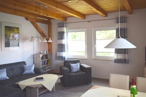 A living room with a sofa, armchair, table, bookshelf, and a bottle of wine. - Terraced house with 2 bedrooms (Ostseebad Prerow)