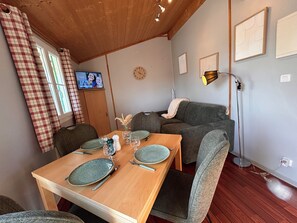 A dining area with a wooden table set for four, a sofa, and a television displaying a program.