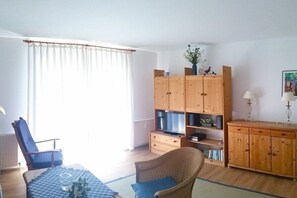 Ein Wohnzimmer mit Fernseher, Holzschränken, einem Sessel und einem Tisch mit einer Vase.