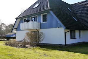 Ein zweistöckiges Haus mit Balkon, geneigtem Dach und einem kleinen Garten.