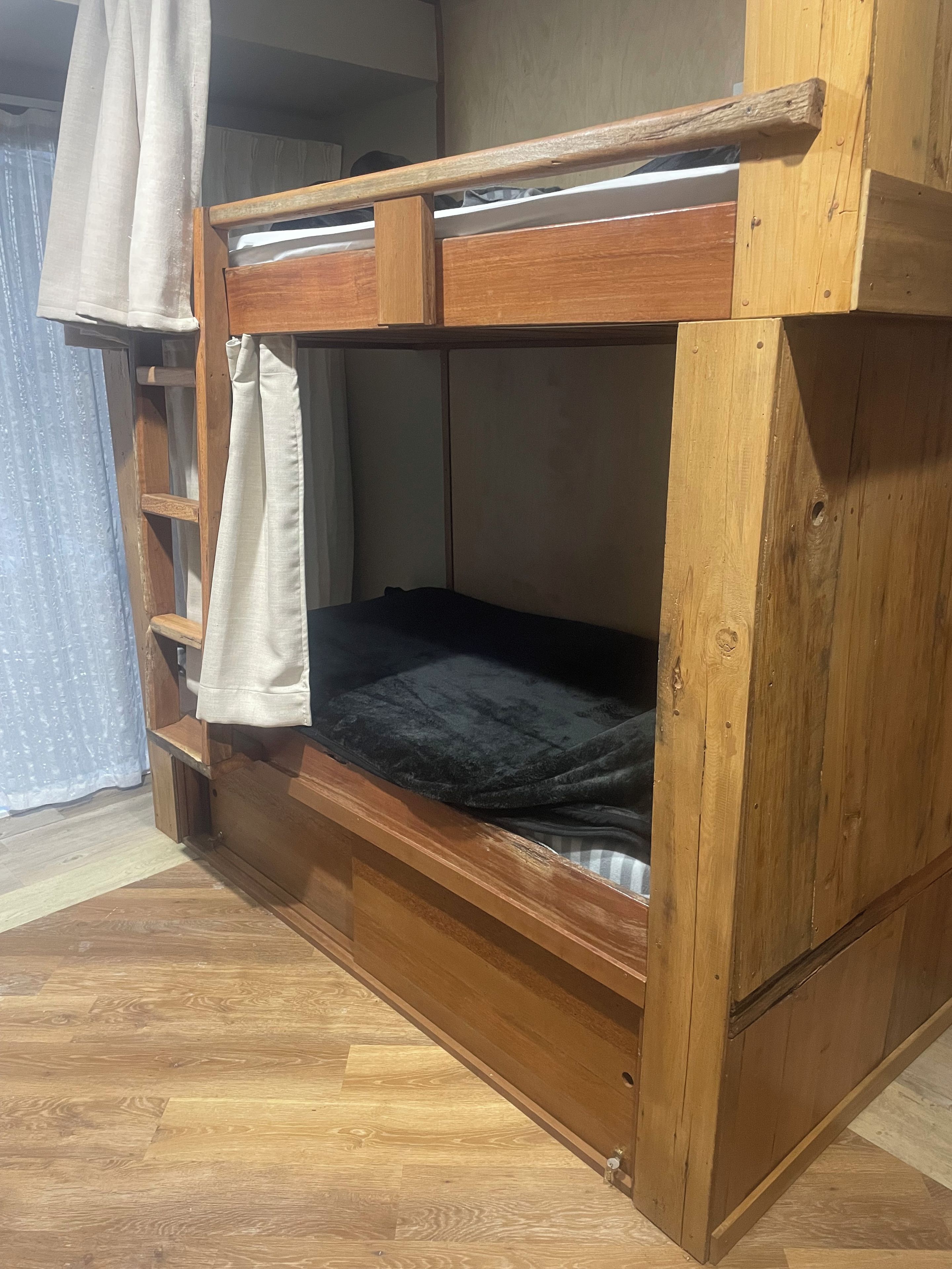 A bunk bed with a wooden frame, a lower shelf, and a curtain.