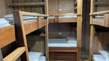 Ein Schlafraum mit Etagenbetten, Holzwänden und Holzdielen, einem Einzelbett in der Mitte und einer kleinen Bank.