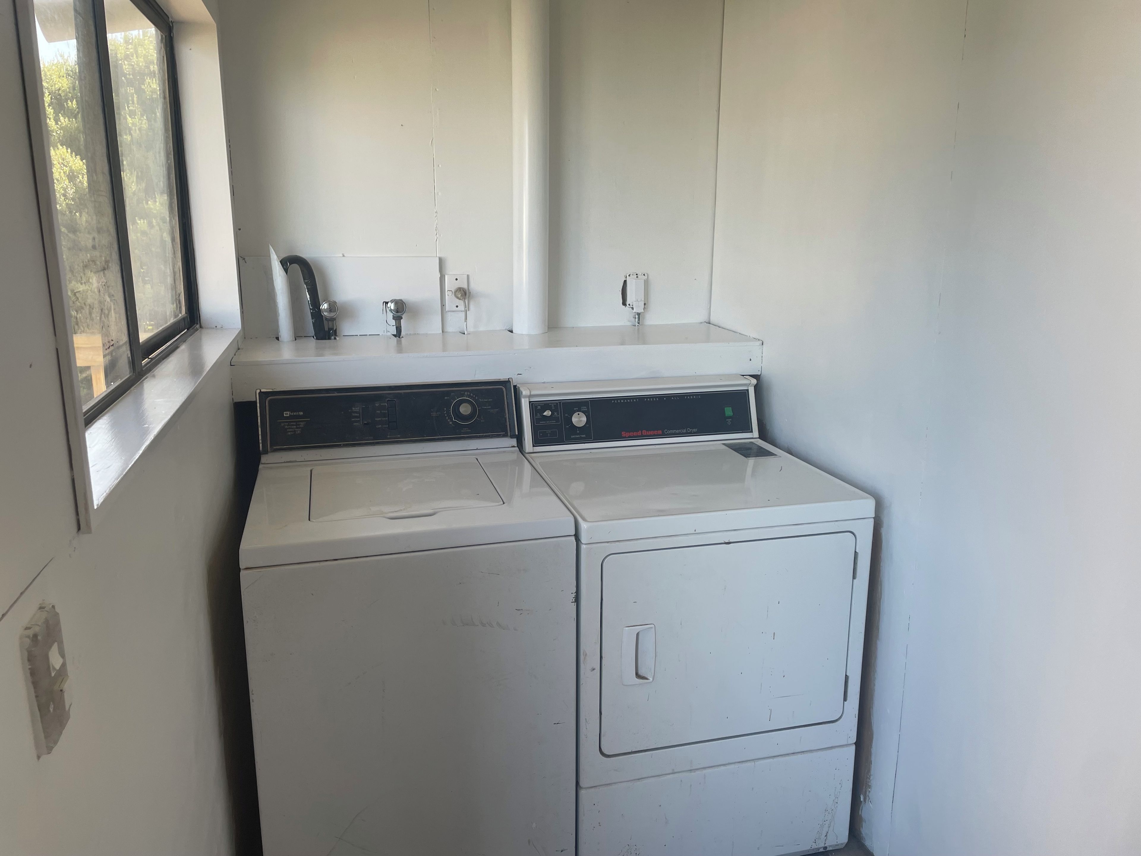 A laundry room with two stacked washers and dryers, a window, and a white wall.