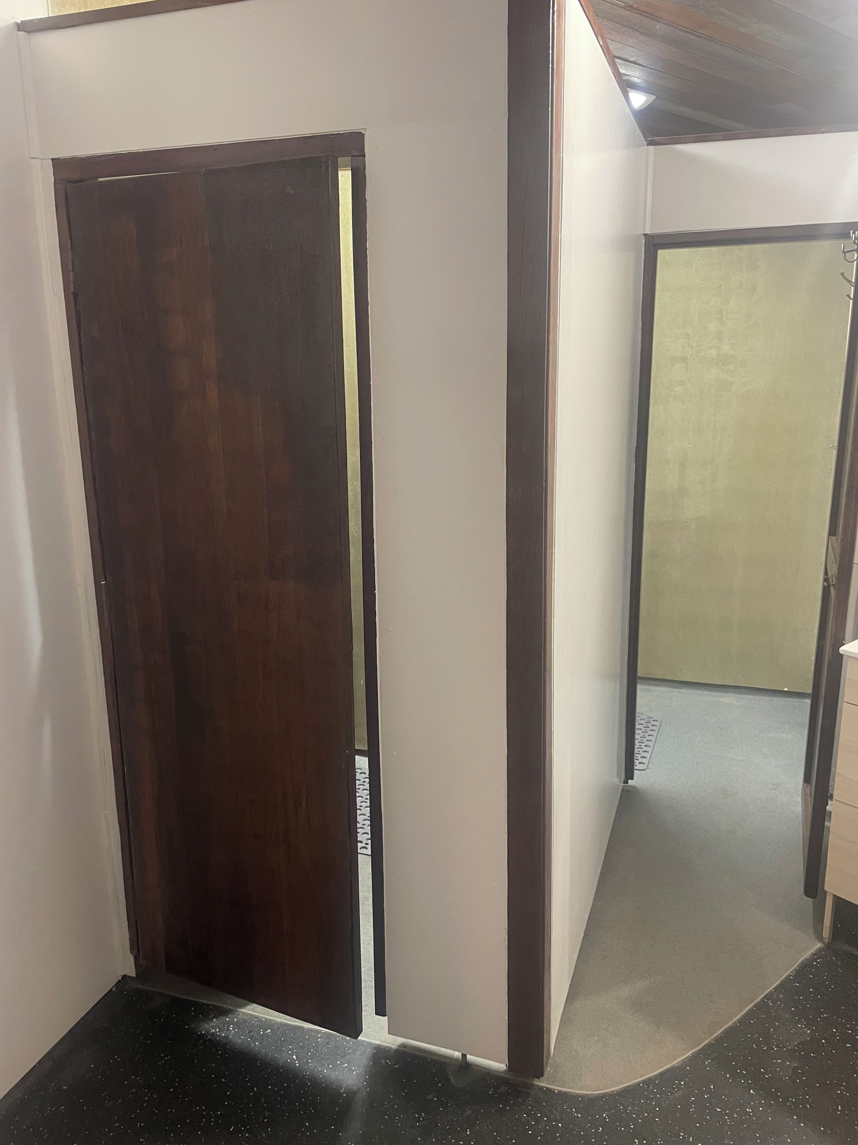 A hallway with a wooden door, a white wall, and a grey floor.