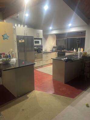 A modern kitchen with stainless steel appliances, a central island, and a red-tiled floor.