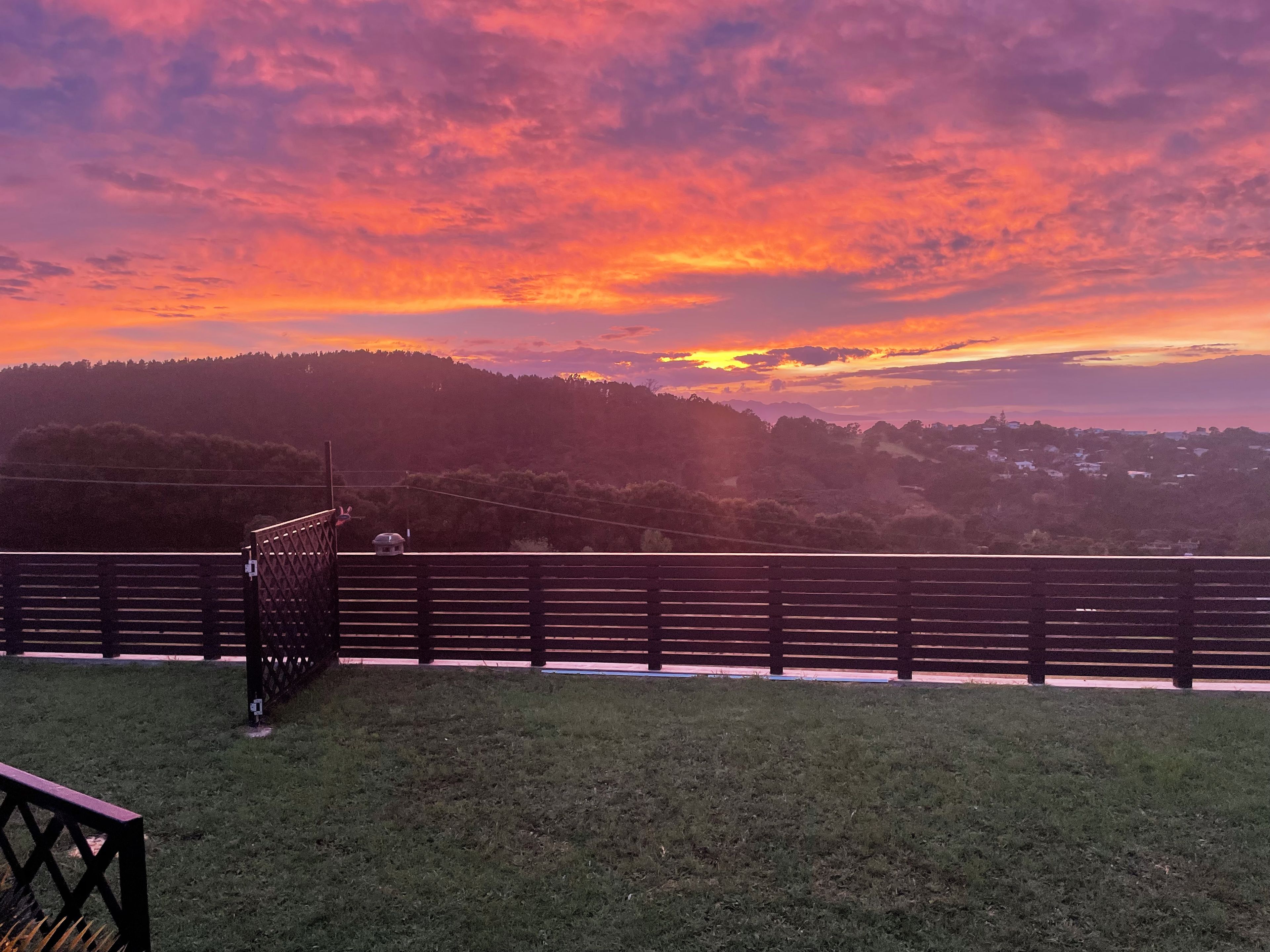 A sunset view from a grassy area with a wooden fence in the foreground.